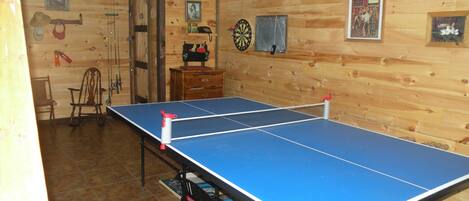 Una mesa de ping pong en una habitación con paredes de madera, un dardo y un pequeño armario de madera.