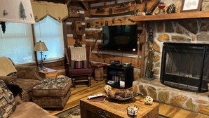 Ein gemütliches Wohnzimmer mit Kamin aus Stein, einem Fernseher und einem Holztisch.