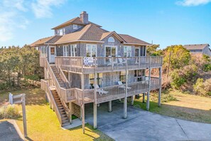 A two-story beachfront house with a balcony, a staircase, and a sign indicating a surf sound level of 113. - Spacious Oceanview Home in Frisco with Hot Tub, Screened Porch. Beach Nearby! (Frisco)
