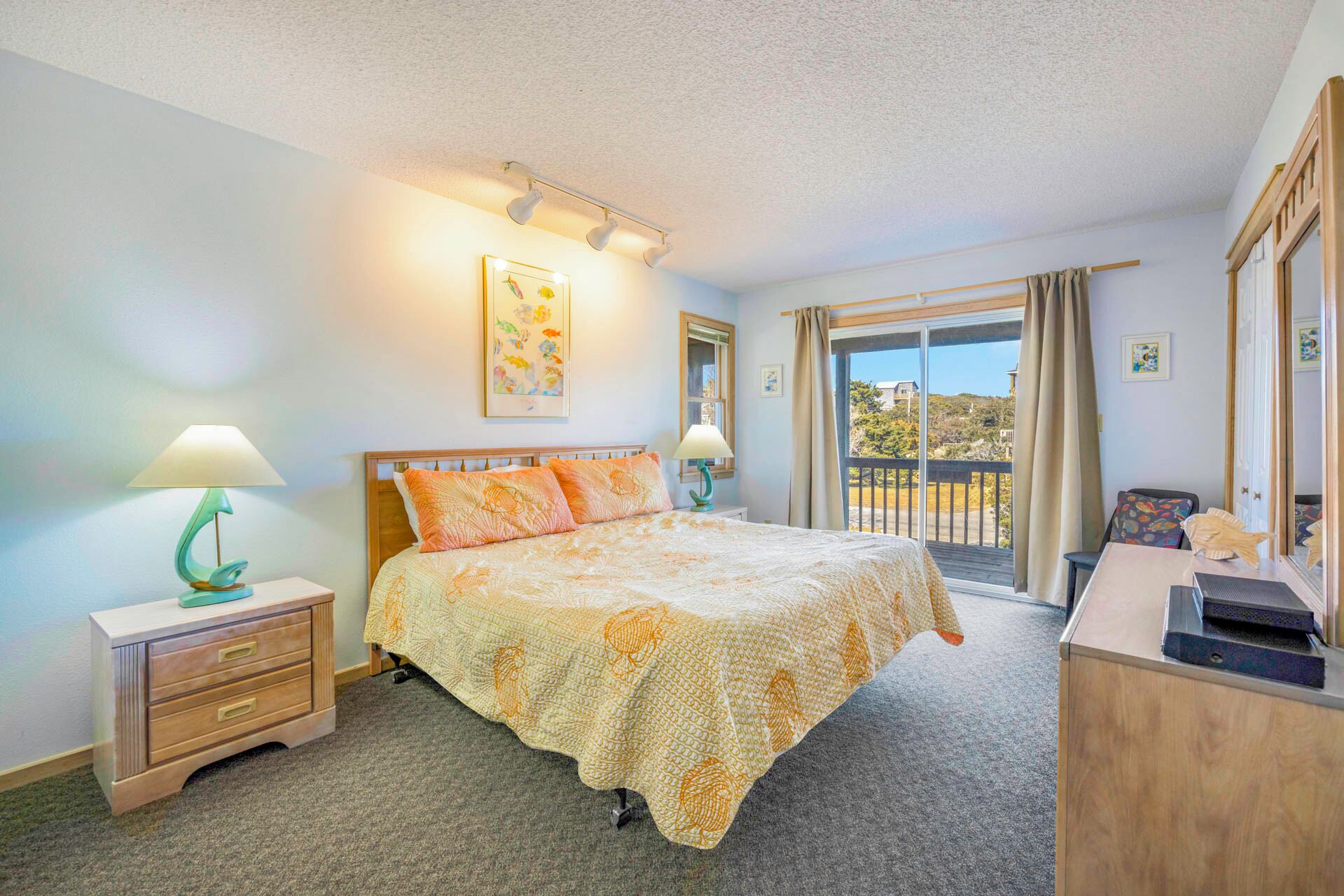 A bedroom with a bed, two bedside tables with lamps, a dresser, a window with curtains, and a balcony.