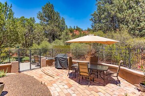 Une terrasse extérieure avec une table et des chaises, un barbecue abrité et une clôture en métal.