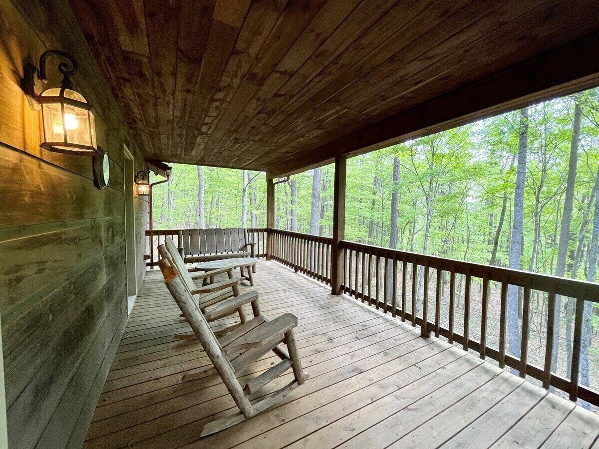 A covered wooden deck with benches, a railing, and a view of a forest.