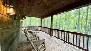 A covered wooden deck with benches, a railing, and a view of a forest.