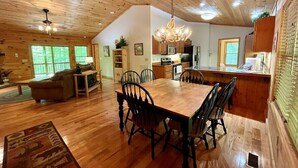 A spacious living area with a wooden dining table and chairs, a sofa, and a chandelier.