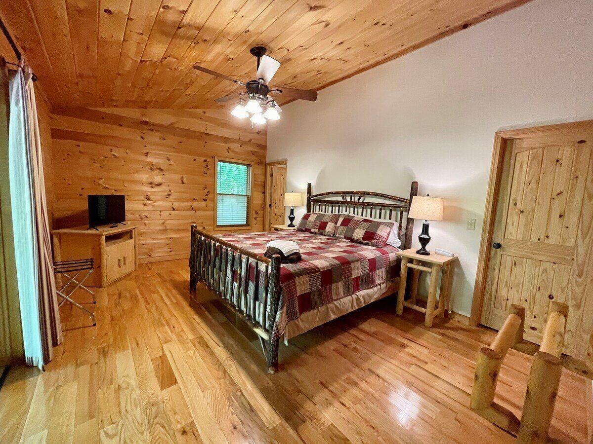 A wooden cabin bedroom with a bed, a ceiling fan, a window, and a door.