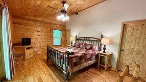 A wooden cabin bedroom with a bed, a ceiling fan, a window, and a door.