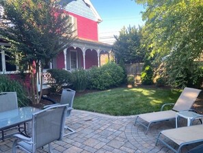 A patio area with a stone floor, metal chairs, and a red building in the background.