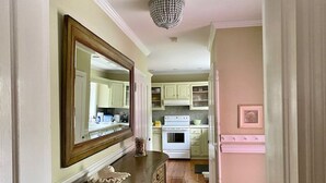 A hallway leading to a kitchen with white cabinets, a white stove, and a large mirror on the wall. - Welcome to the iconic Pink Lady (Lewes)