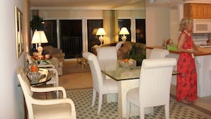 A dining area with a glass table and white chairs, a kitchen with a microwave, and a woman in a red dress.
