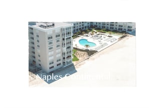 Um edifício alto com piscina no terraço e área ajardinada com palmeiras.