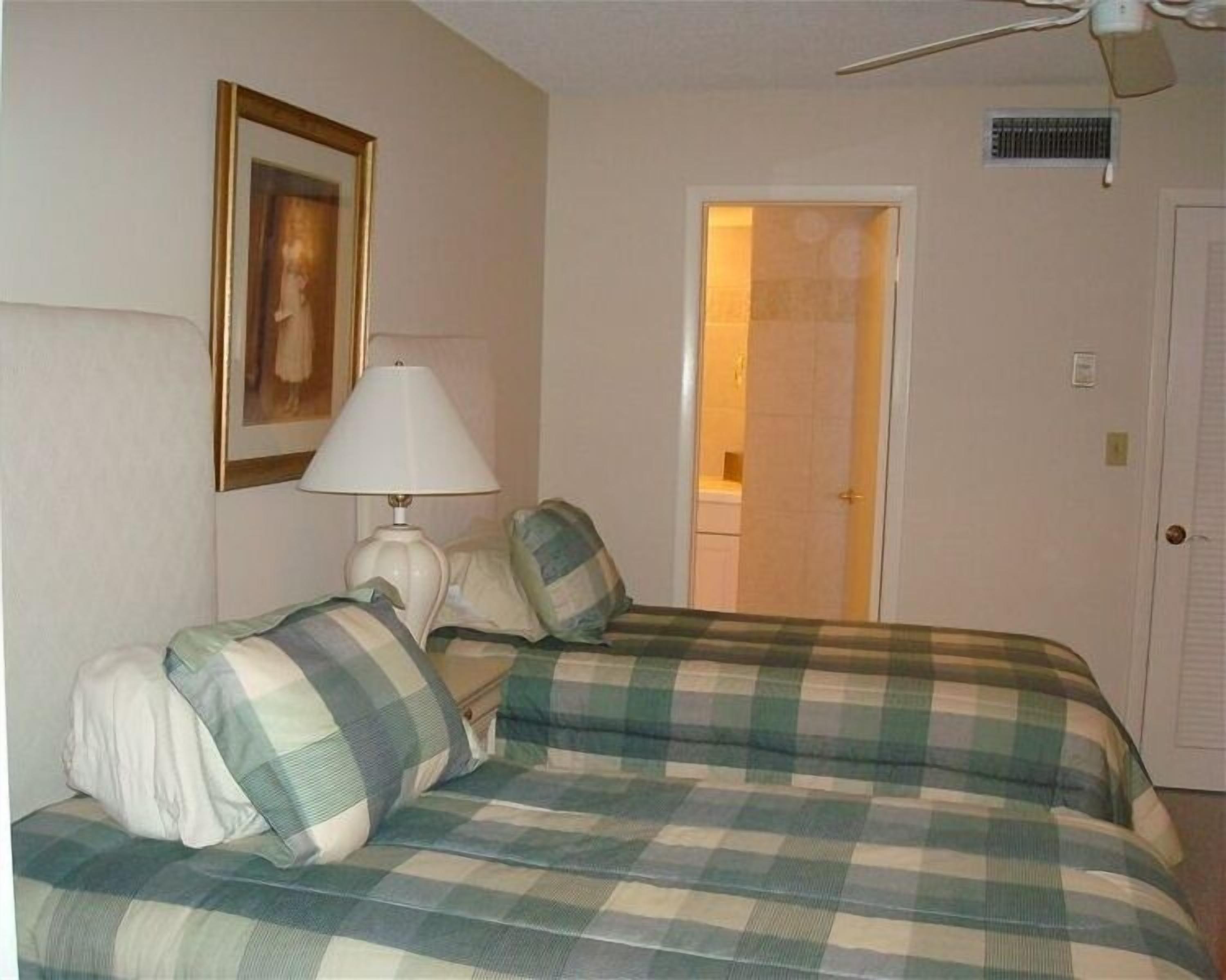 Une chambre d’hôtel avec un lit, une lampe, un tableau au mur et une porte donnant sur une autre pièce.