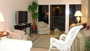 A living room with a sofa, armchair, TV, and a glass table.