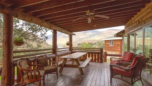A wooden deck with a picnic table and wicker chairs, overlooking a mountainous landscape.