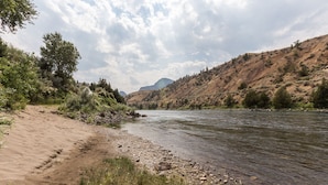 A riverbank with a sandy path, rocky shore, and a mountain in the background.