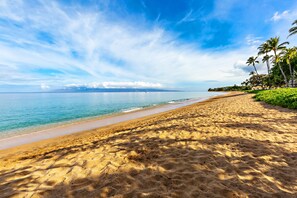 A beach with clear skies, calm waters, and a distant mountain range.