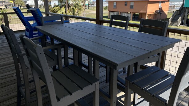 Una terraza de madera con una mesa y sillas, con vistas a una playa y casas.