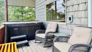 Un espacio al aire libre techado con mobiliario de mimbre, un jacuzzi y vistas a árboles.