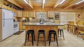Una cocina con armarios de madera, un refrigerador blanco, encimera de granito y un taburete de bar.