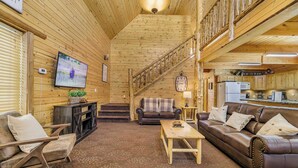 Un interior acogedor con una escalera de madera, una sala de estar con un sofá y televisión, y una zona de cocina.