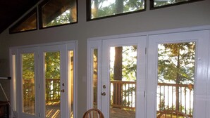 A dining area with a table and chairs, a glass door leading to an outdoor deck, and a view of trees through the door. -  Lake Front Home with community boat ramp. Private,  close to marinas and town. (Somerset)