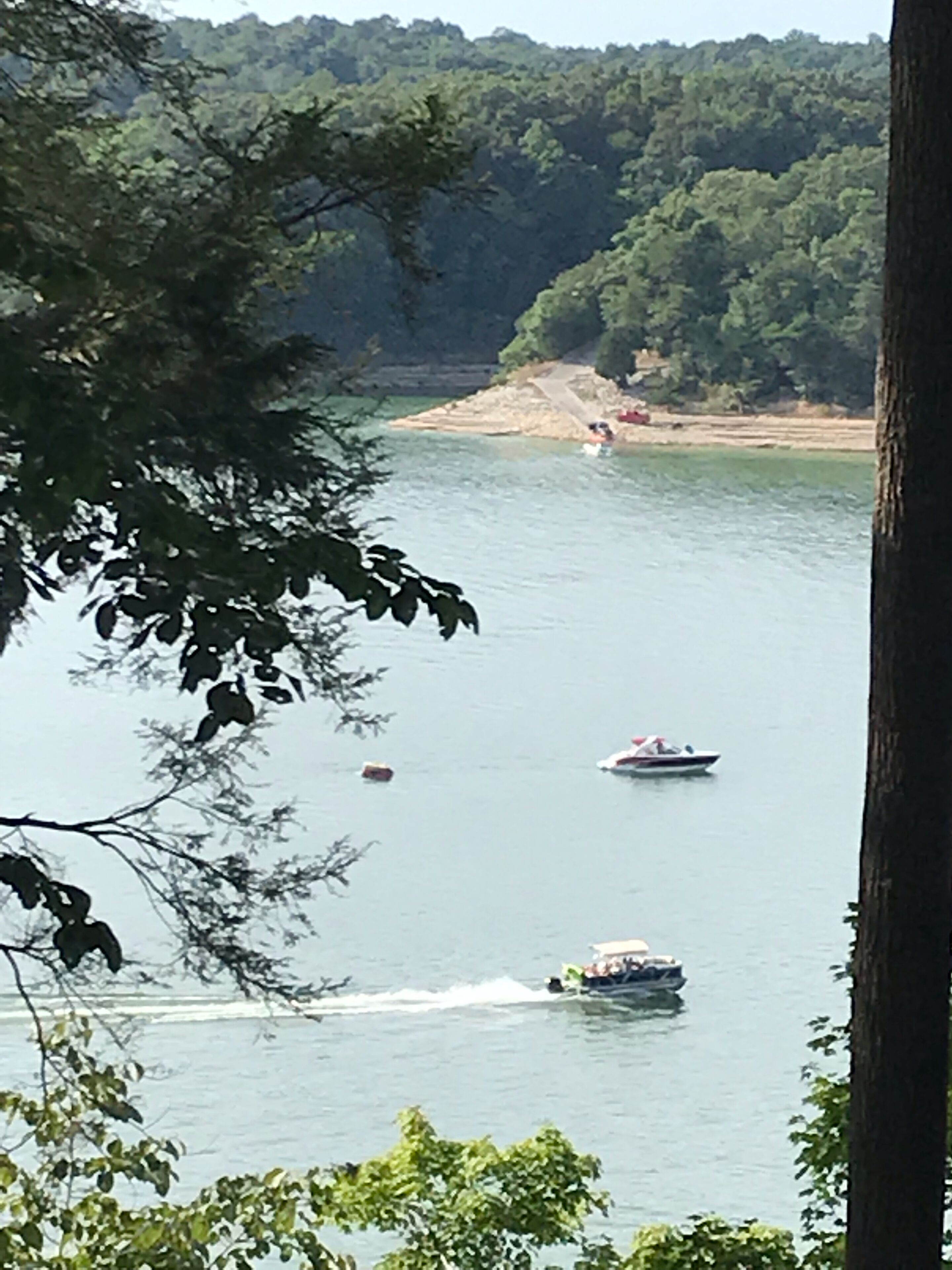 Järvi, jossa on veneitä, ja jonka ympärillä on puita sekä kauempana näkyvä rantaviiva.