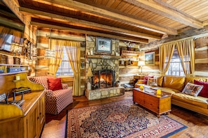 A cozy log cabin interior with a stone fireplace, wooden furniture, and a large patterned rug. - DOGWOOD LODGE • TIMBERIDGE (SPARED)• (Gatlinburg)