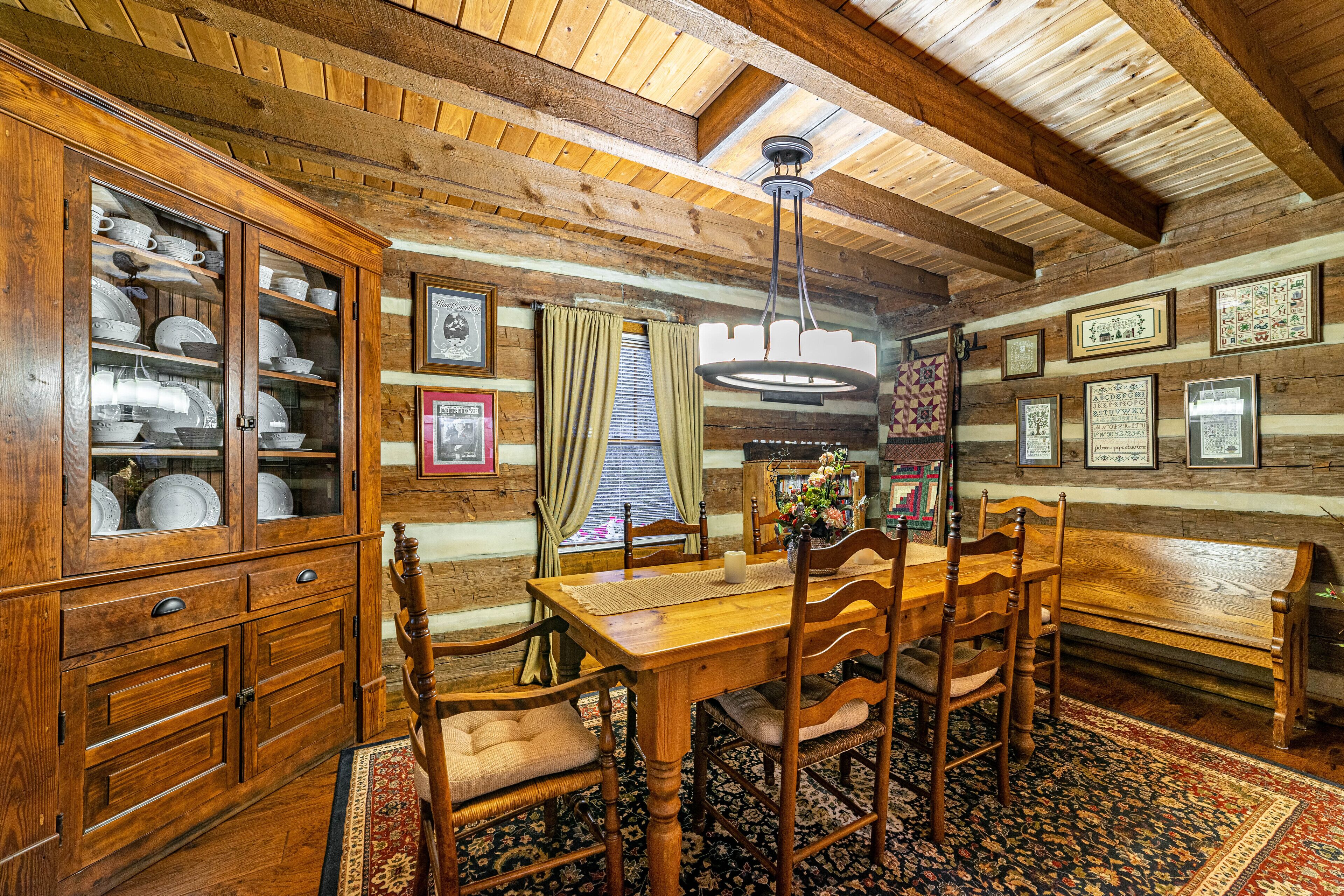 A rustic wooden dining room with a wooden table and chairs, a cabinet with glass doors, and a patterned rug.