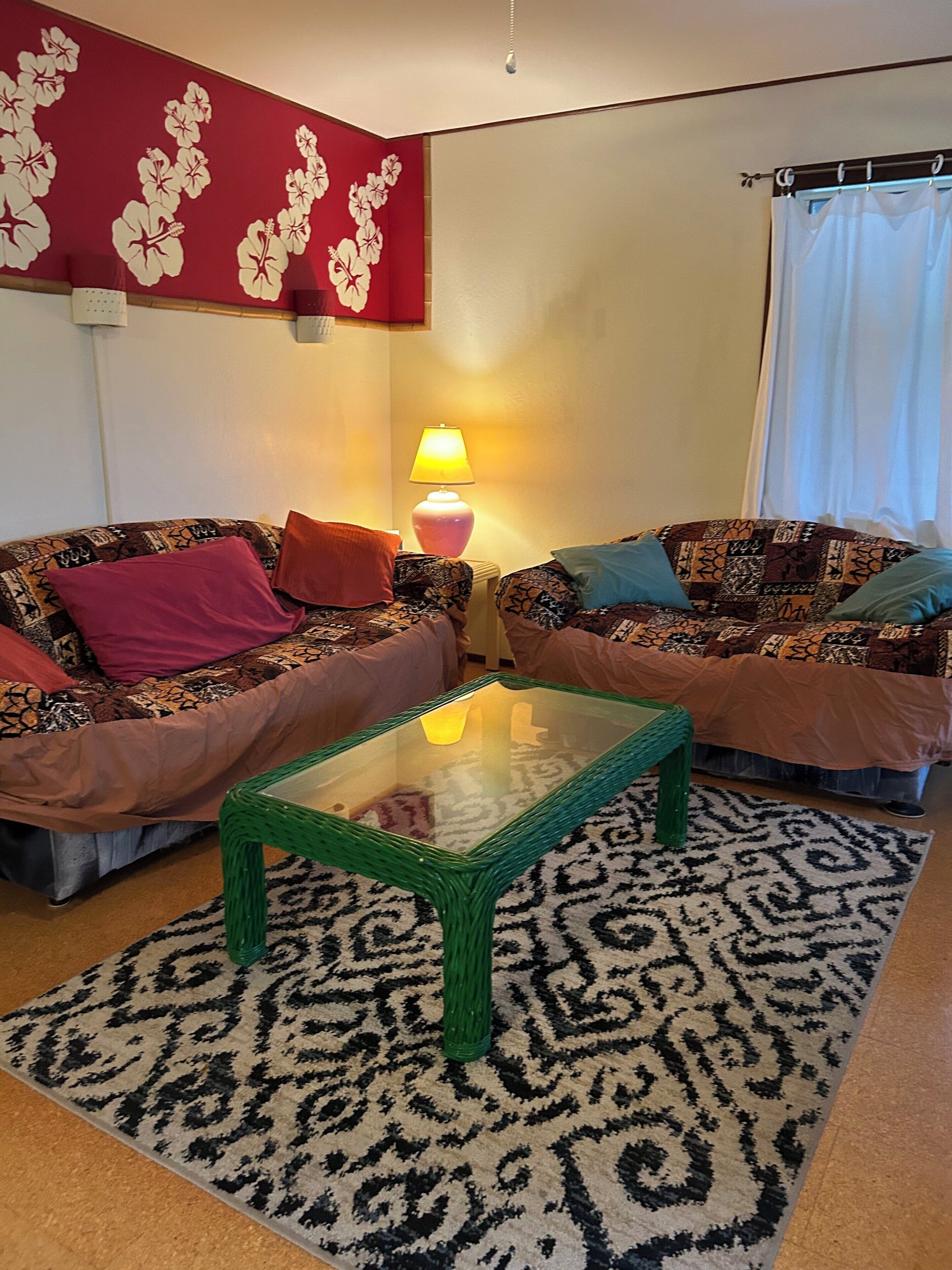Un salon comprenant deux canapés, une table basse en verre, un tapis à motifs et un mur orné d’un motif floral.
