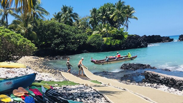 A beach with boats, a rocky shoreline, and palm trees.