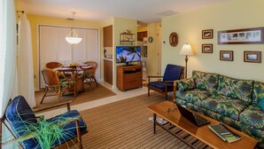 A living room with a sofa, coffee table, TV, and dining area with chairs and a table.