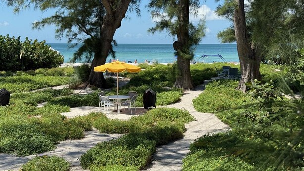 A pathway leading to a beach area with a yellow umbrella and white chairs.