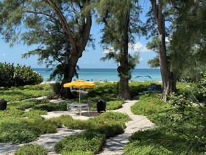 A pathway leading to a beach area with a yellow umbrella and white chairs. - Gulf-side 1BR--75 Steps to Sand, Private Patio, Family-Owned Since 1971 (Holmes Beach)