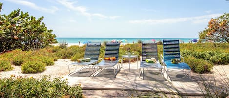 A beachside lounge area with sun loungers, a small table with drinks, and a view of the ocean.