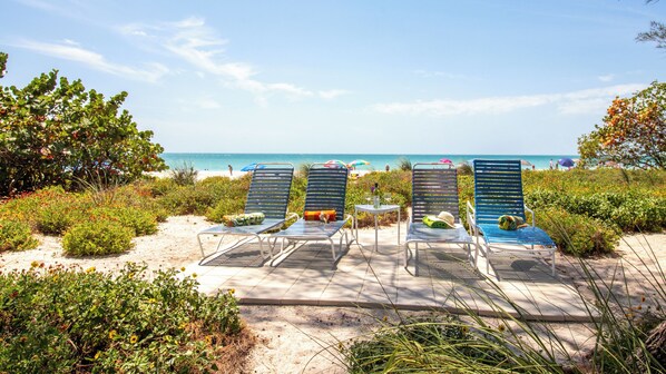 A beachside lounge area with sun loungers, a small table with drinks, and a view of the ocean.