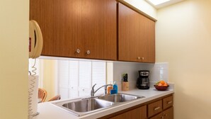 A kitchen with wooden cabinets, a stainless steel sink, a coffee maker, and a bowl of fruit on the counter.