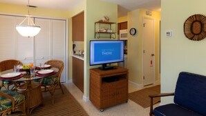 A dining area with a table set for four, a television on a stand, and a living room with a blue sofa.
