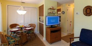 A dining area with a table set for four, a television on a stand, and a living room with a blue sofa.