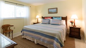 A bedroom with a bed, two bedside tables with lamps, a chair, a window with curtains, and a painting on the wall.