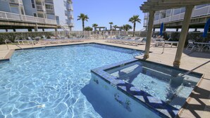 Une piscine à l’eau claire, entourée de chaises longues et de parasols, avec un immeuble à plusieurs étages en arrière-plan.