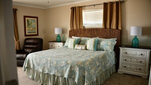 A bedroom with a large bed, two nightstands, a chair, and a window with curtains. - Bettie's Beach House (Mexico Beach)