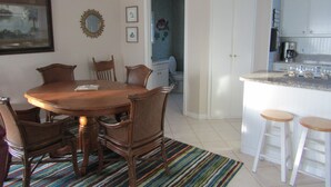 A dining area with a wooden table and chairs, a colorful striped rug, and a kitchen with white cabinets and stools. - Bettie's Beach House (Mexico Beach)