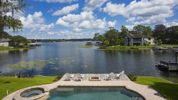 A swimming pool with lounge chairs, a dock, and a view of a lake with boats. - Lakefront Pool Home w/ Game Room, Epic View, Kayaking (Tampa)