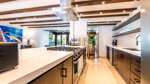 Eine moderne Küche mit einer zentralen Kochinsel, Edelstahlgeräten und Holzbalken an der Decke.
