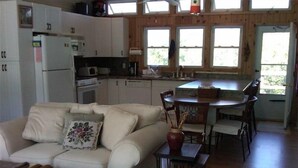 Una sala de estar acogedora con un sofá, una mesita y un comedor con sillas. Hay una cocina con armarios y un refrigerador.