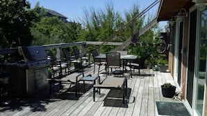 Una terraza de madera con mobiliario exterior, una parrilla y una planta en maceta.