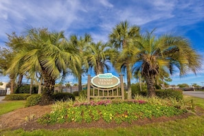 A sign for 'Searscape Tennis Village' with palm trees and a landscaped garden.