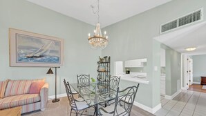 Ein Essbereich mit einem Glastisch, Metallstühlen, einer Chandelierleuchtre, einem gerahmten Gemälde und einem gestreiften Sofa.