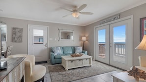 A living room with a ceiling fan, a lighted sign reading "Welcome to the Porch", a lighted lamp, a blue sofa with decorative pillows, a coffee table, and a wicker basket.