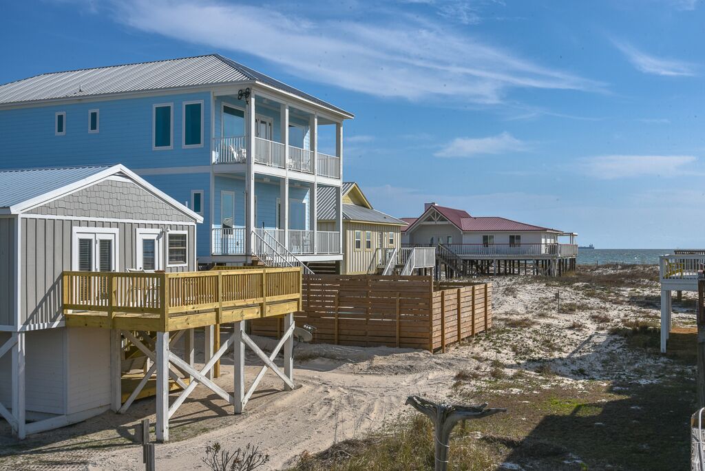 Een strandhuis met een galerij over twee verdiepingen, een houten terras en een zandstrand op de achtergrond.