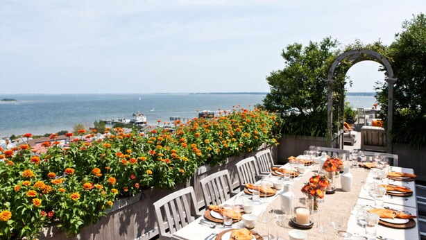 An outdoor dining area with a view of the sea, tables set with plates and glasses, and a flower wall. - 1 Bedroom Cottage in the Old Historic District. Free Street Parking.  (Charleston)